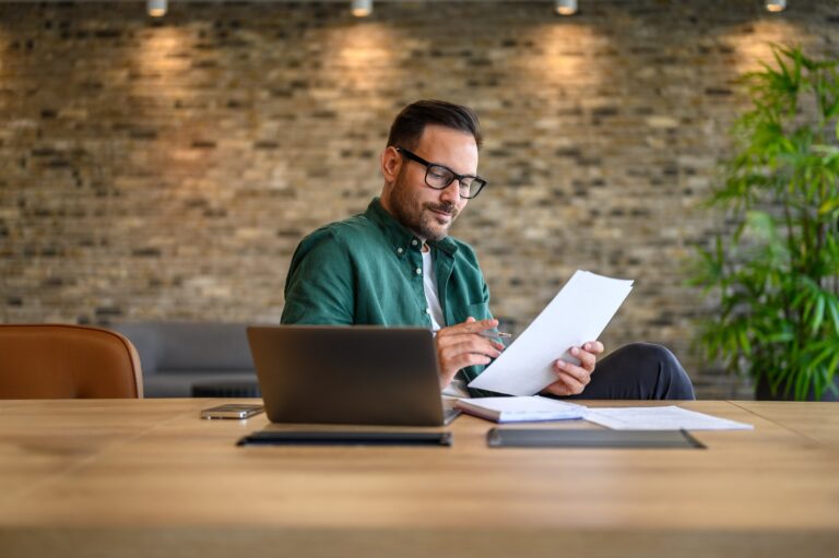 Advogado analisa documentos em um escritório, com um notebook na mesa, representando a facilidade de solicitar certidões online com o Plano Corporativo da Central de Certidões.